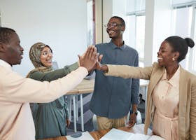 A joyful group of diverse colleagues high-fiving each other in an office, symbolizing teamwork and collaboration.